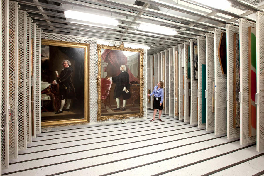 Mujer observando grandes pinturas hist&#243;ricas en almacenamiento.