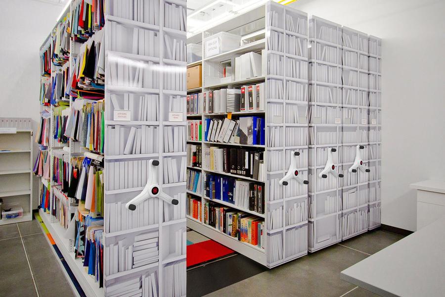 Estanter&#237;as m&#243;viles de alta densidad en un espacio de oficina, llenas de carpetas y documentos, optimizando el almacenamiento.
