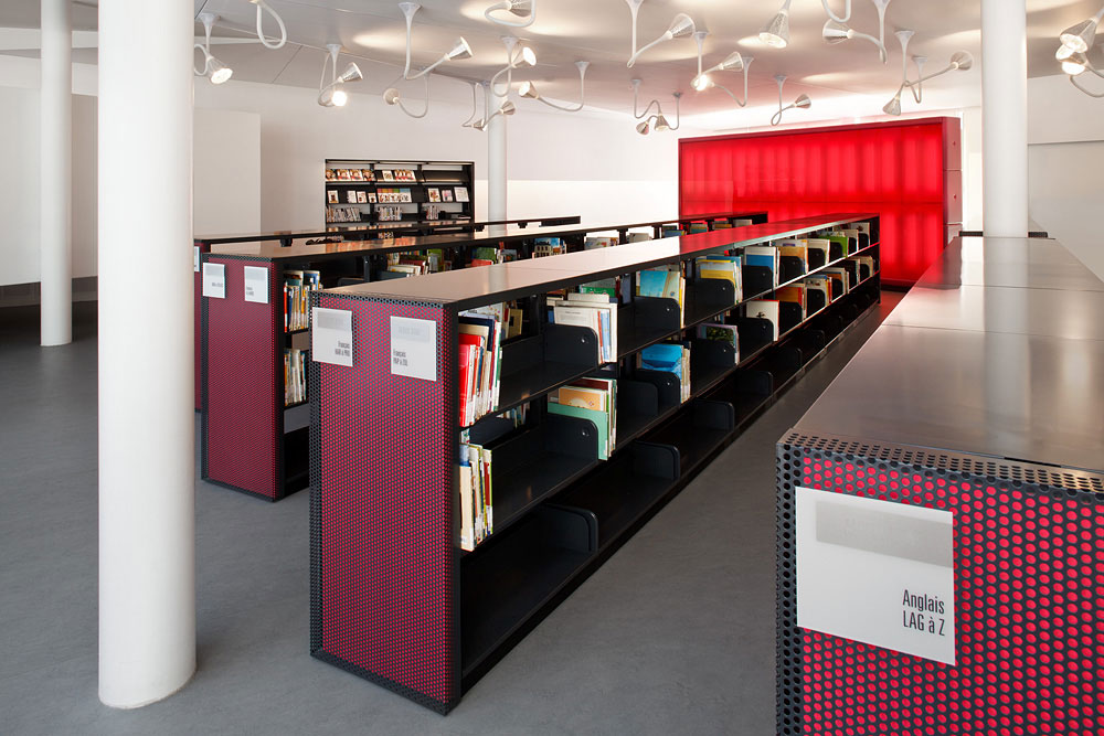 Biblioteca con estantes rojos y libros coloridos en una sala de lectura moderna.