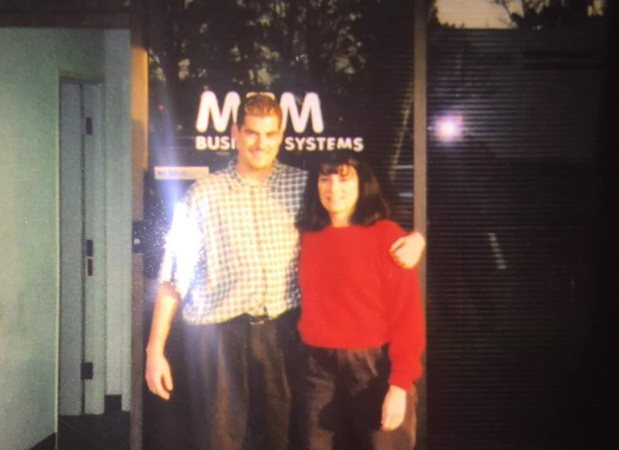 Photo of an old photograph of two people in front of the M&amp;M Business Systems building.